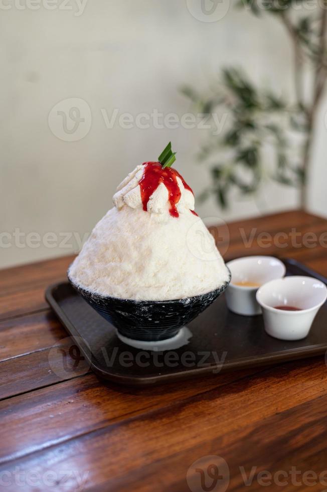postre de hielo raspado coreano con coberturas dulces, bingsu de fresa en mesa de madera foto
