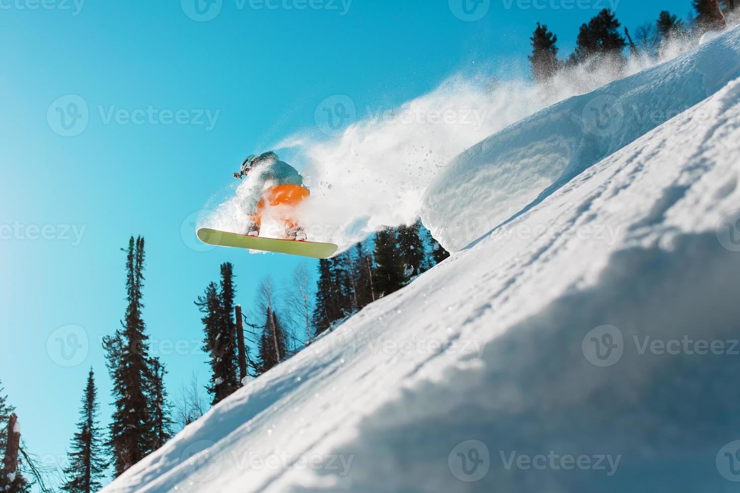 Snowboarder jumps from a high snow-covered springboard in a forest against a blue sky photo