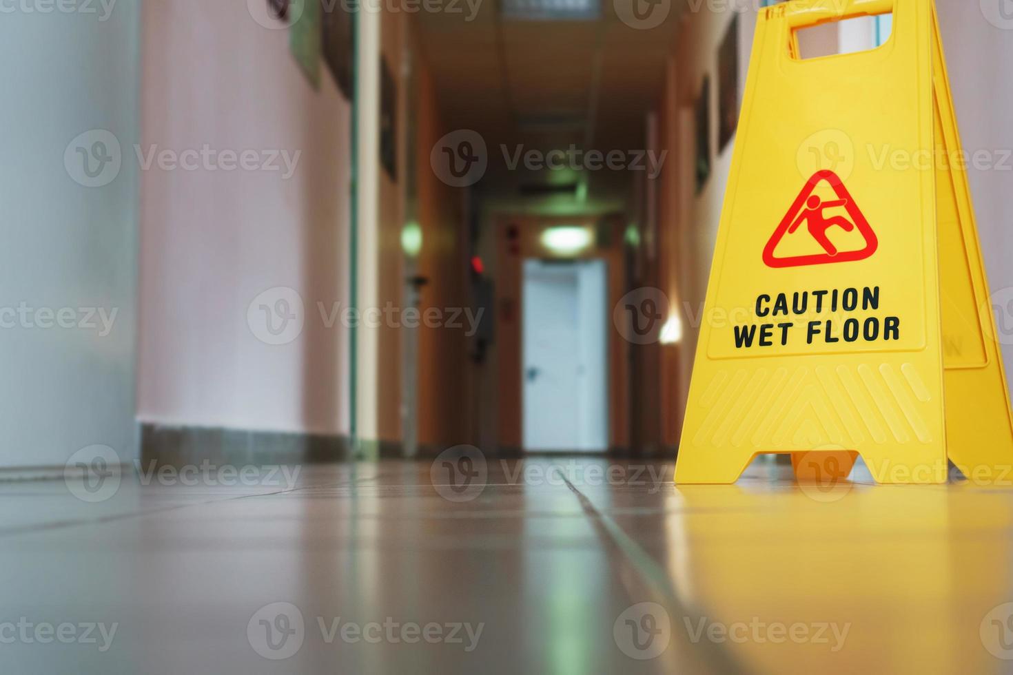 A sign that reads Caution is a long empty industrial corridor. Yellow sign of slippery floor in the room after cleaning. photo