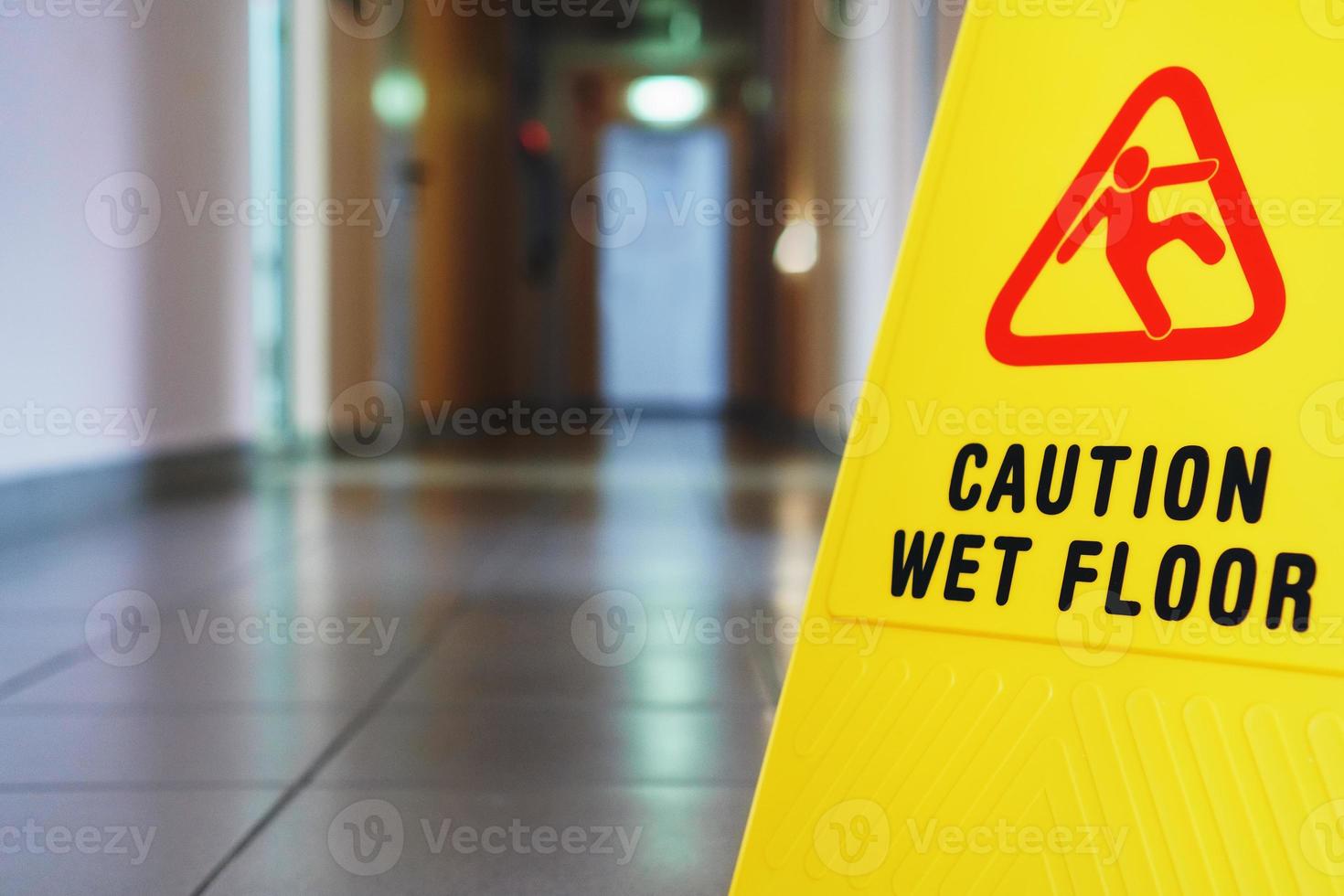 A sign that reads Caution is a long empty industrial corridor. Yellow sign of slippery floor in the room after cleaning. photo