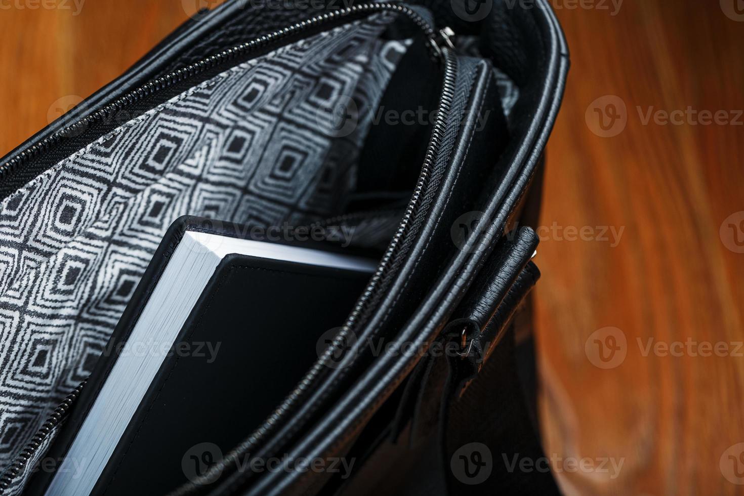 Black notebook peeking out of the pocket of a black leather bag close-up, macro Handmade, natural materials. photo