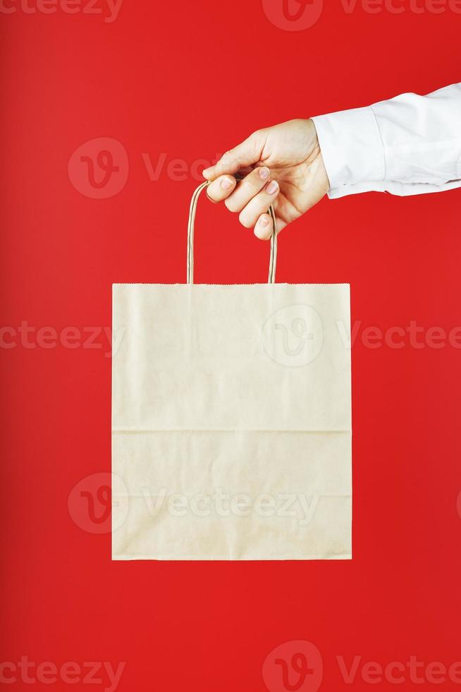 Paper bag at arm's length isolated on a red background. Layout of the packaging template with space for copying, advertising. photo