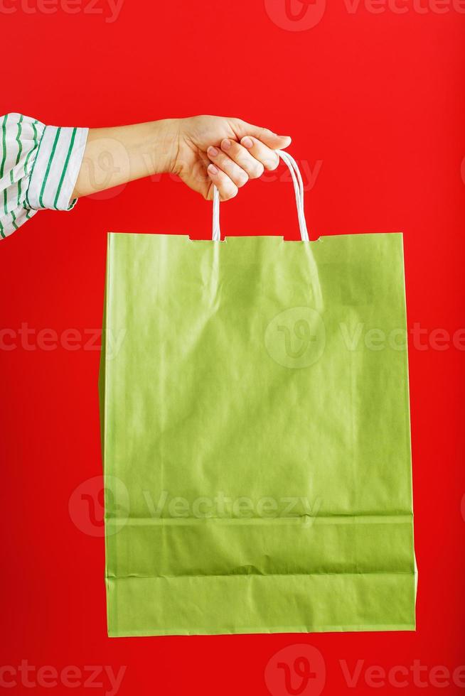 Green paper bag at arm's length isolated on a red background. Layout of the packaging template with space for copying, advertising. photo