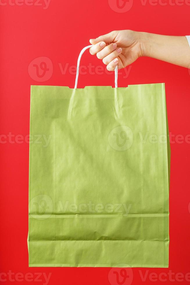 Green paper bag at arm's length isolated on a red background. Layout of the packaging template with space for copying, advertising. photo