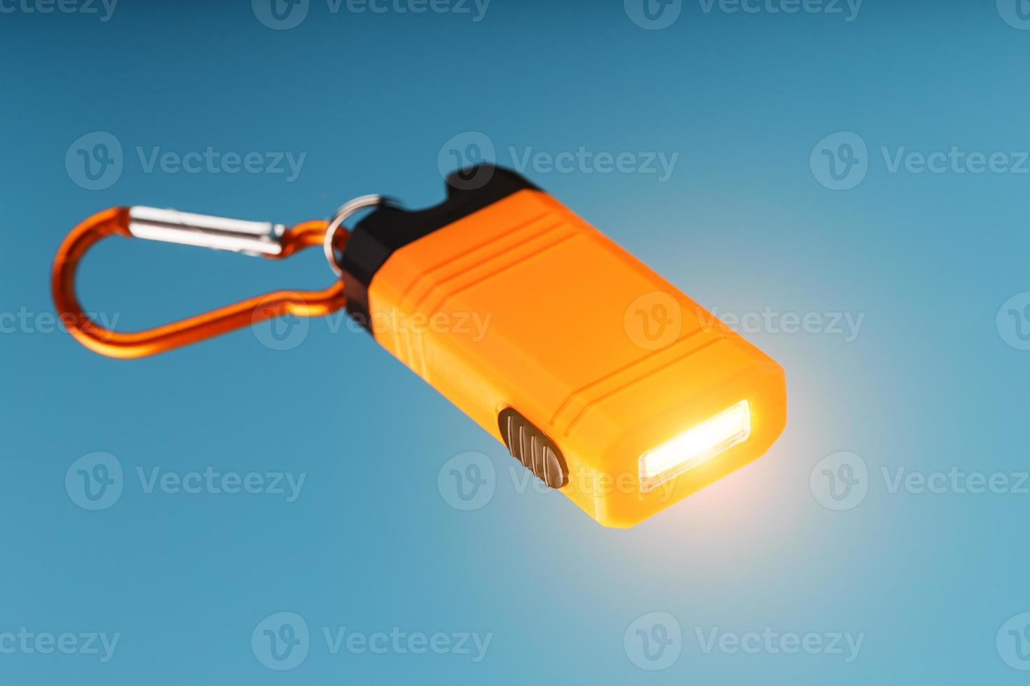 An orange led flashlight with a carabiner glows on a blue background. photo