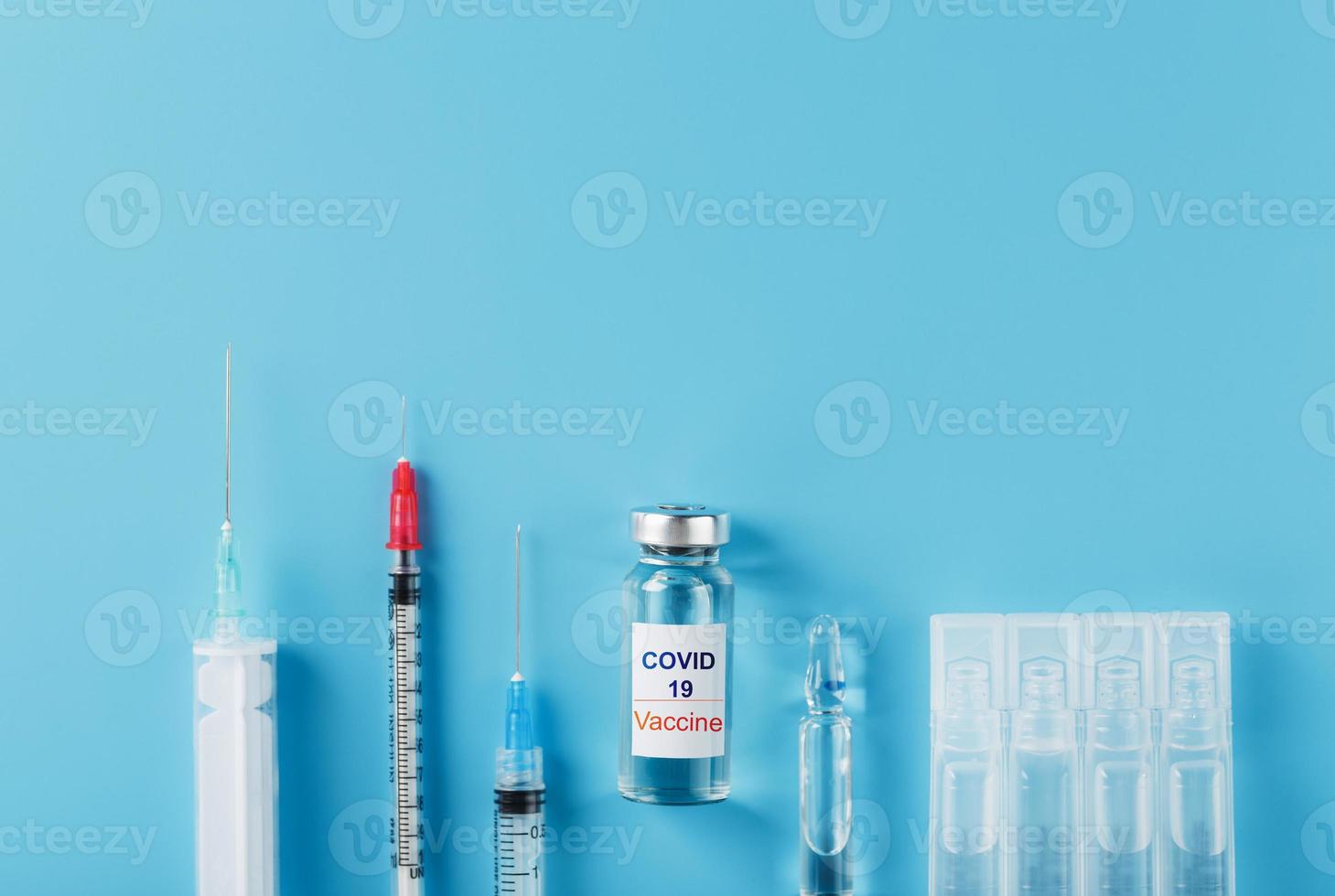 A set of ampoules with the inscription Covid-19 vaccine and a set of syringes against a blue background. photo