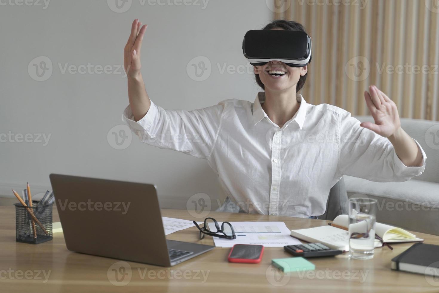 alegre joven mujer de negocios moviendo las manos en el aire mientras usa gafas de realidad virtual en el lugar de trabajo foto