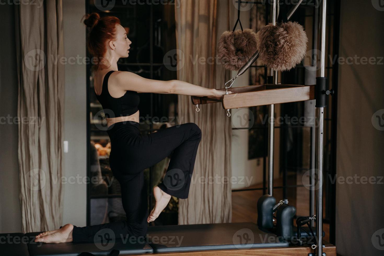 Young pilates instructor with athletic body exercising on cadilac reformer photo