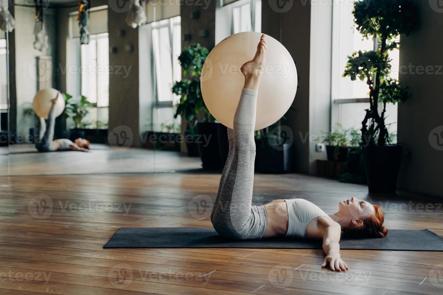 mujer joven haciendo ejercicios para las piernas con pelota de pilates mientras está acostada en la alfombra de yoga foto