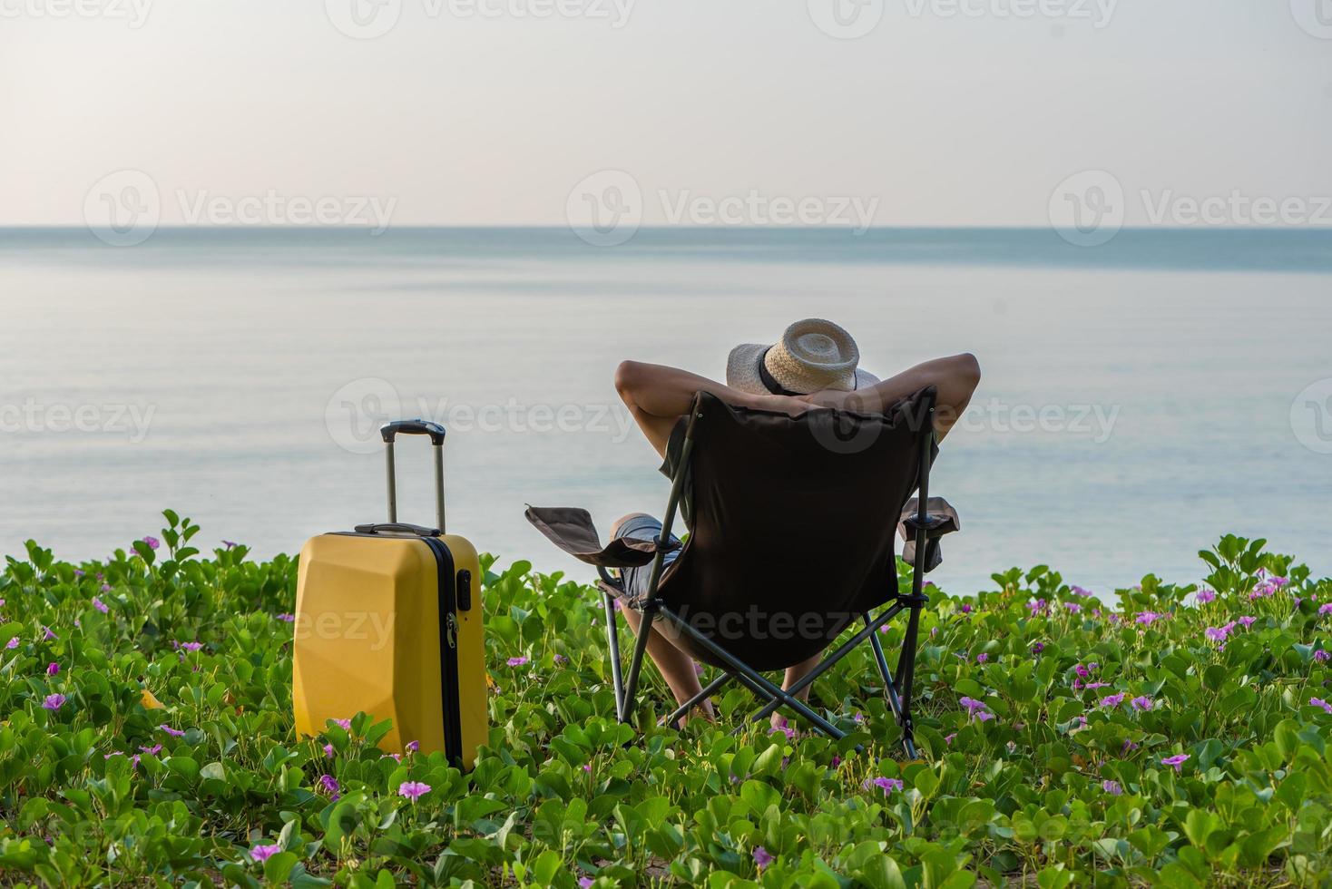 Man sitting on the chair beside suitcase at the beach, vacation, relaxing time concept. photo