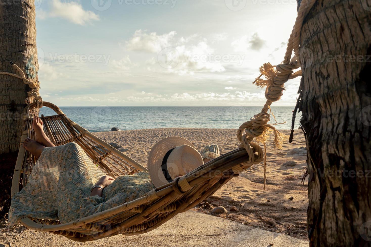 Beautiful young asian woman with hat relaxing relaxing in a hammock between palm trees, Summer happy beach vacation concept. photo