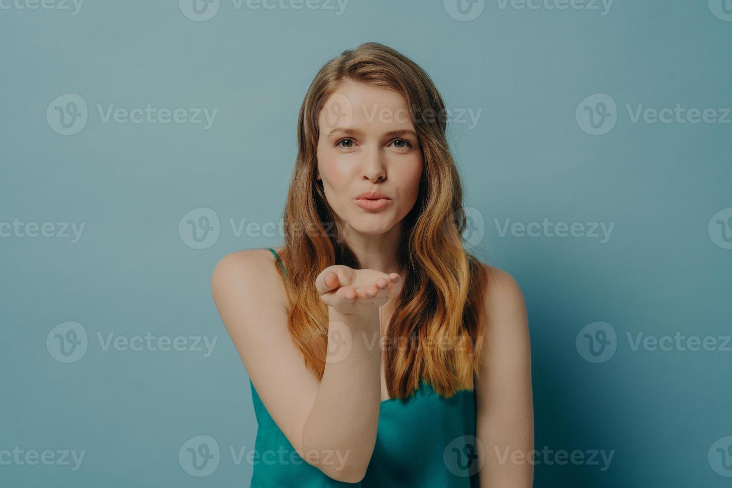 Pretty candid girl blowing air kiss and expressing love while standing isolated on blue background photo