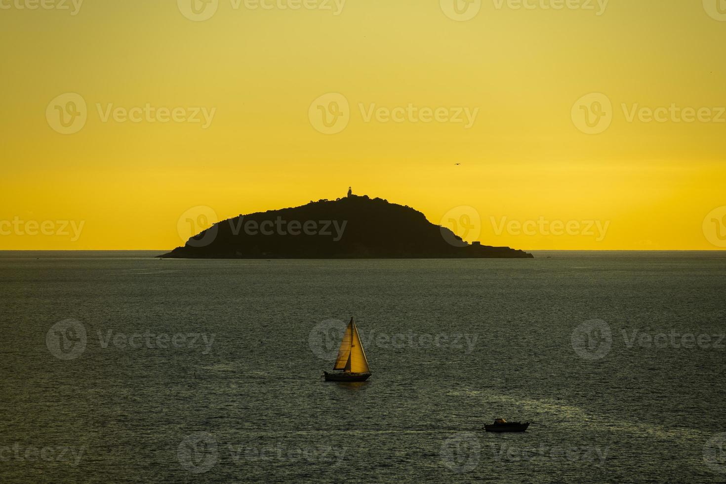 puesta de sol en el mar con isla y velero en silueta foto
