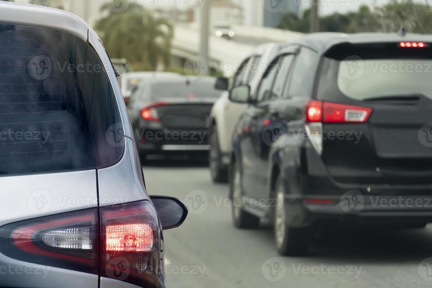 Rear side of silver car on the asphalt road turn on brake light and heading towards the goal of the trip. Traveling for work during rush hour. Environment blurred of other cars during the day. photo