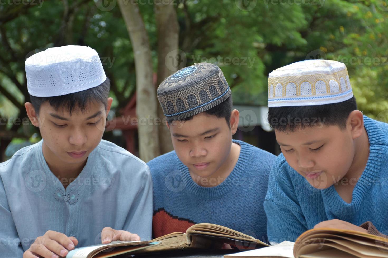 jóvenes asiáticos musulmanes o islámicos sentados juntos en el parque escolar para leer, aprender, hacer y consultar la tarea y esperando aprender temas religiosos en la escuela, enfoque suave y selectivo. foto