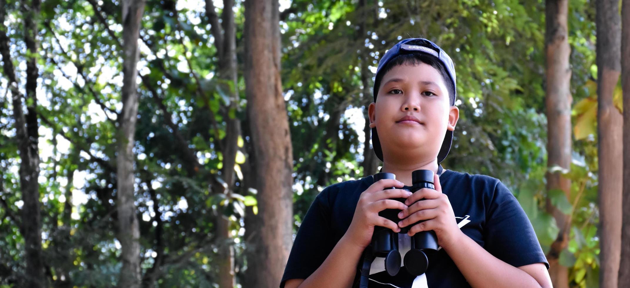 Southeast Asian boys are using binoculars to observe birds in tropical forest, idea for learning creatures and wildlife animals outside the classroom. photo