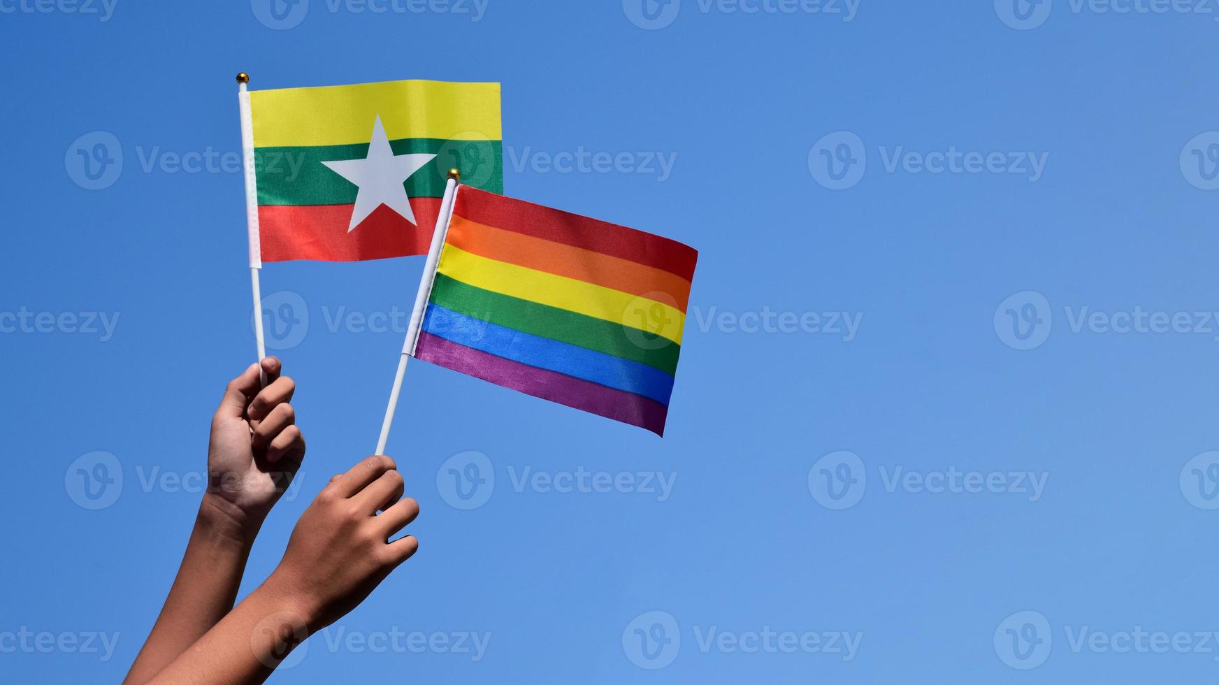 Myanmar and rainbow flags, LGBT symbol, holding in hands, bluesky background, concept for LGBT celebration in Myanmar and around the world in pride month, June, soft and selective focus, copy space. photo