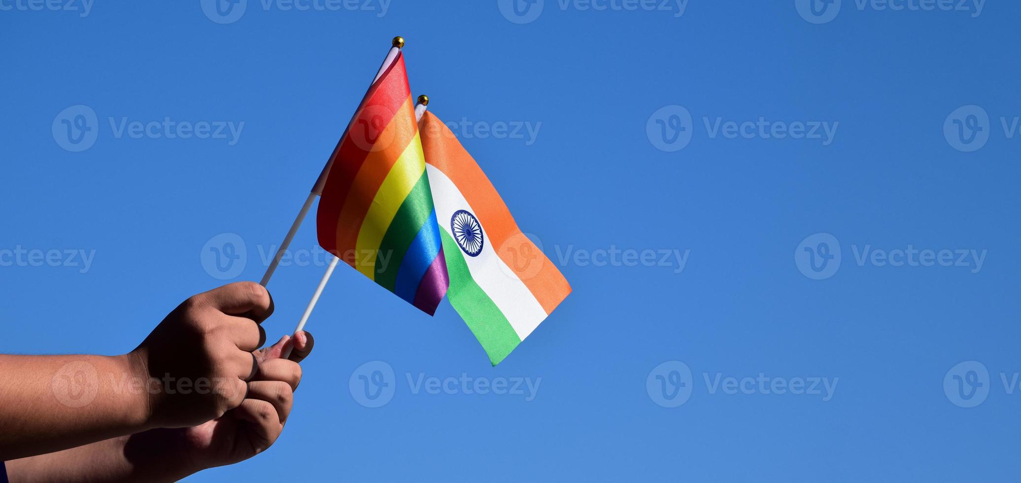 India flag and rainbow flag, LGBT symbol, holding in hands, bluesky background, concept for LGBT celebration in India and around the world in pride month, June, soft and selective focus, copy space. photo