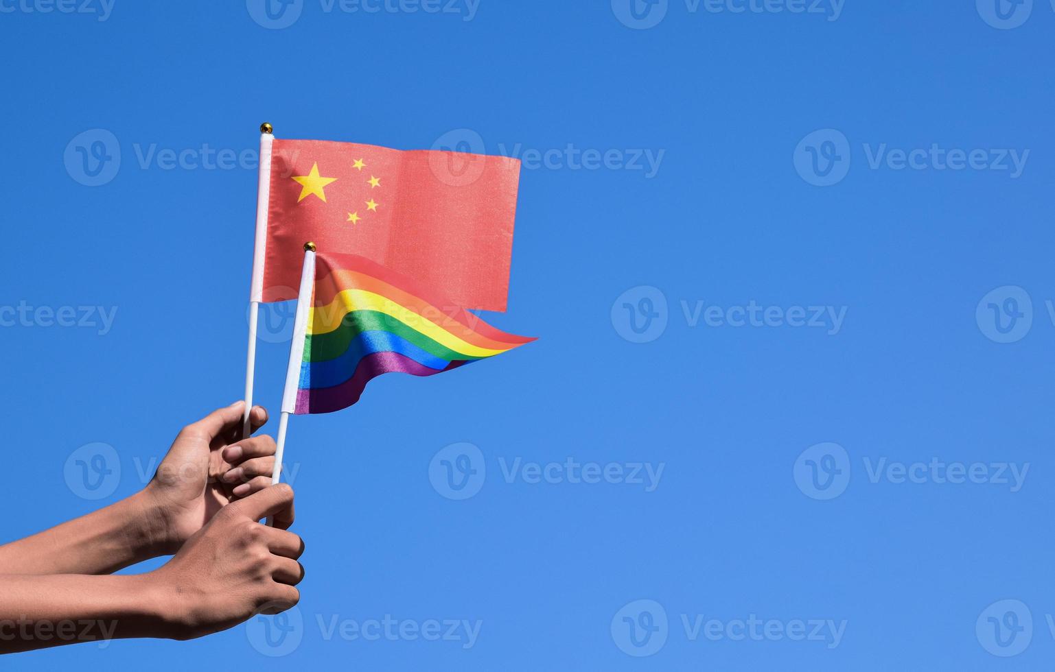 China flag and rainbow flag, LGBT symbol, holding in hands, bluesky background, concept for LGBT celebration in China and around the world in pride month, June, soft and selective focus, copy space. photo