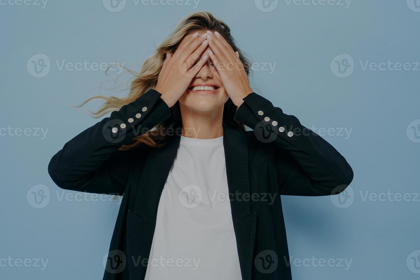 Funny blond beautiful female closing eyes with her hands, having fun and playing hide and seek photo