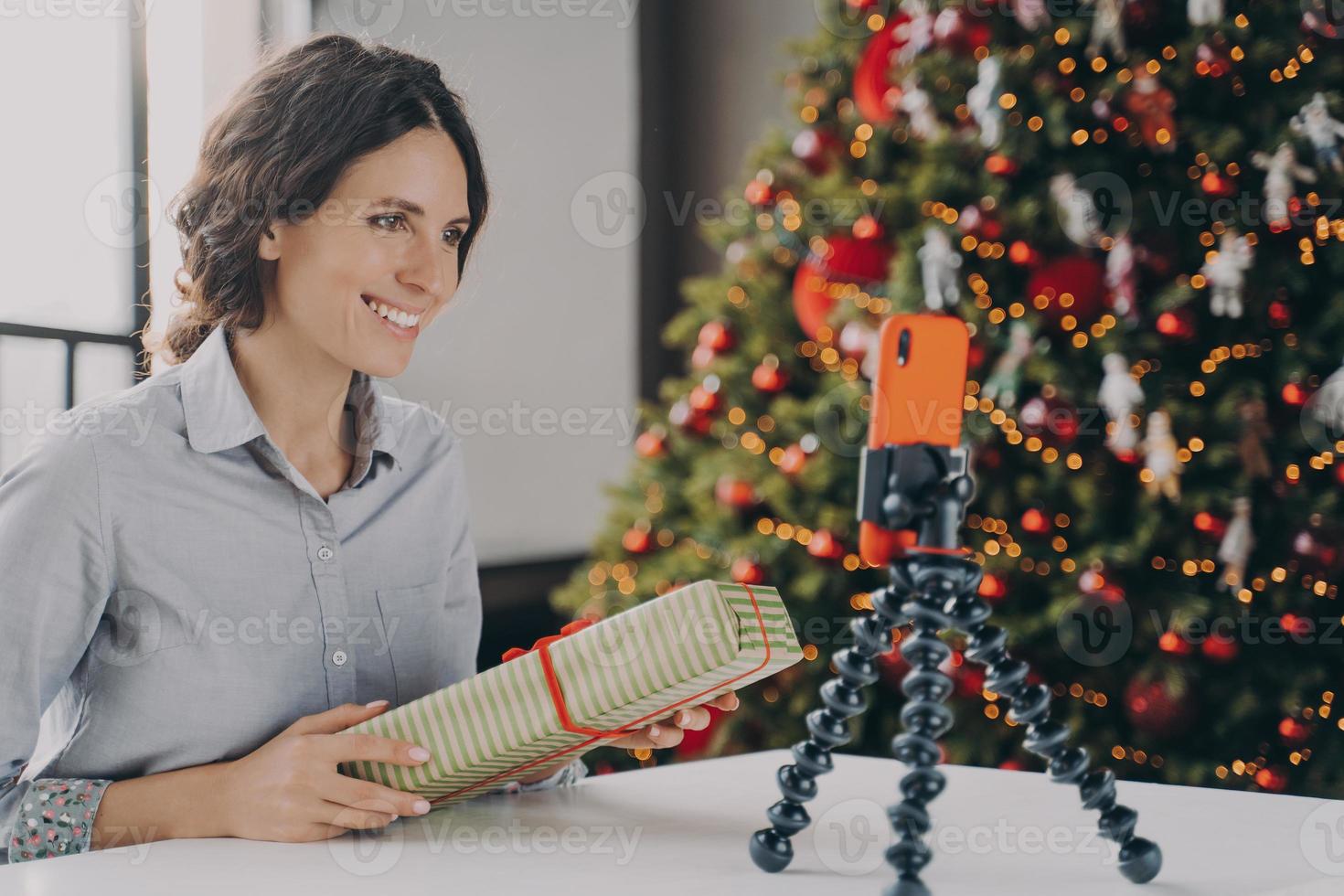Smiling positive female blogger recording video tutorial about tips for wrapping Christmas presents photo