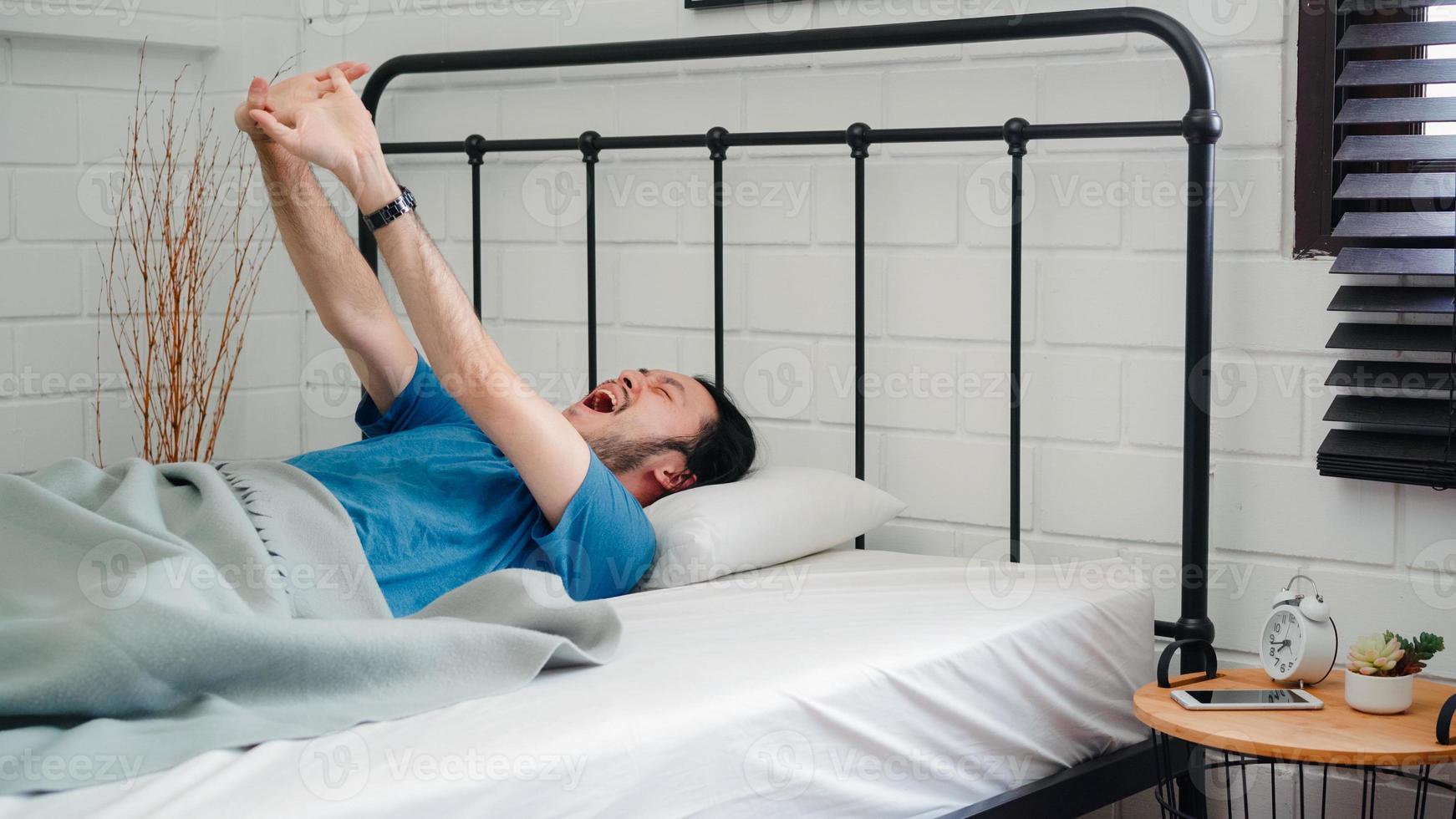 Young Asian man wake up in the morning, male stretching after awake on bed in bedroom at home. Handsome men nap, sleepy relax in modern house concept. photo