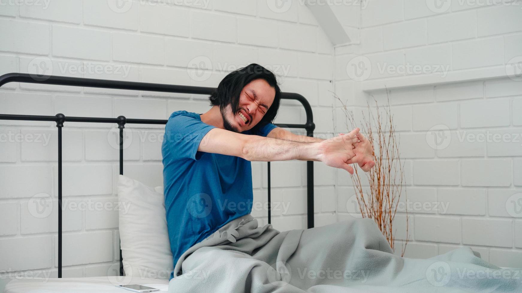 Young Asian man wake up in the morning, male stretching after awake on bed in bedroom at home. Handsome men nap, sleepy relax in modern house concept. photo