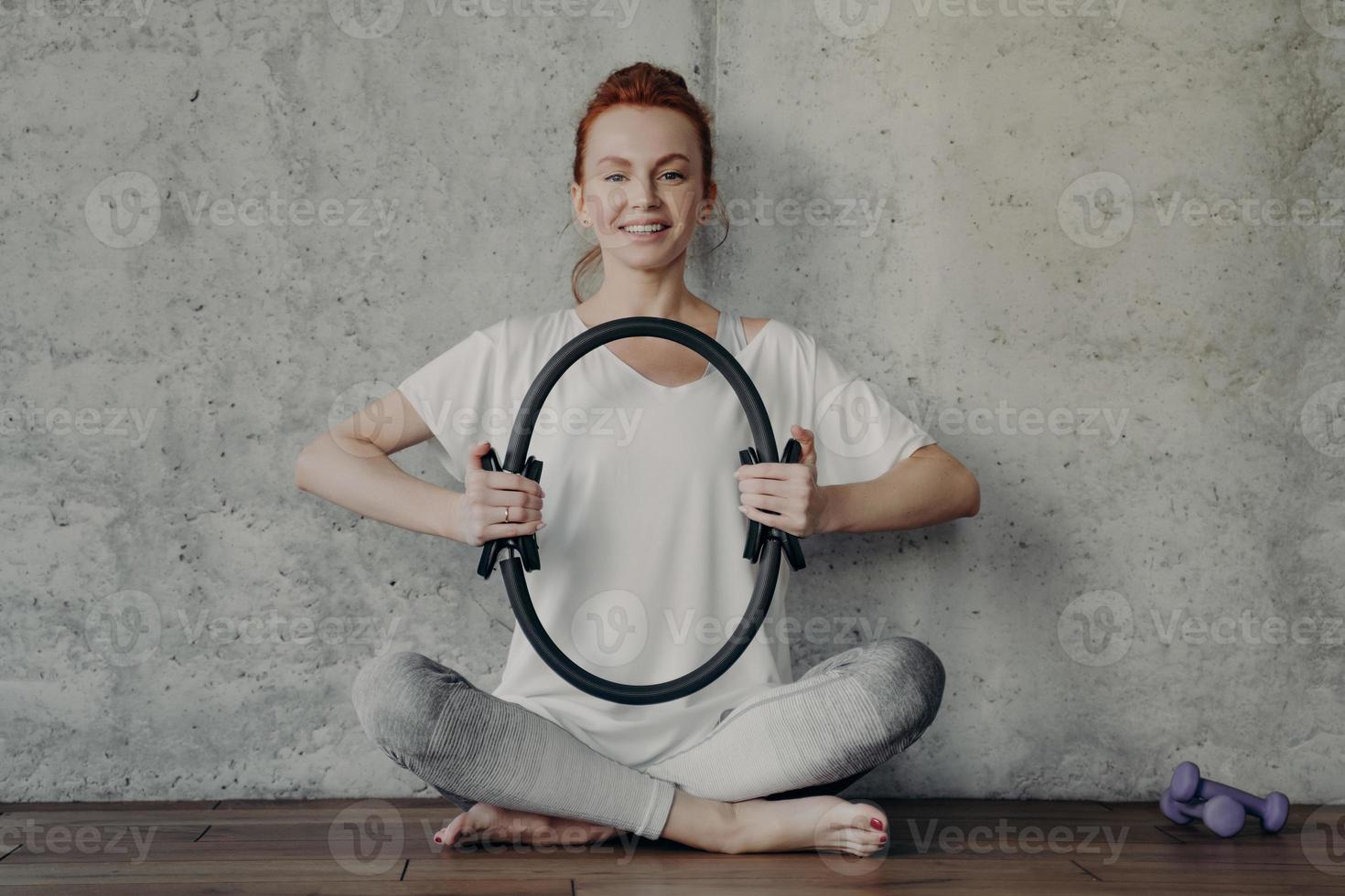 Cheerful fitness woman in active wear sitting in lotus position and exercising with pilates ring photo