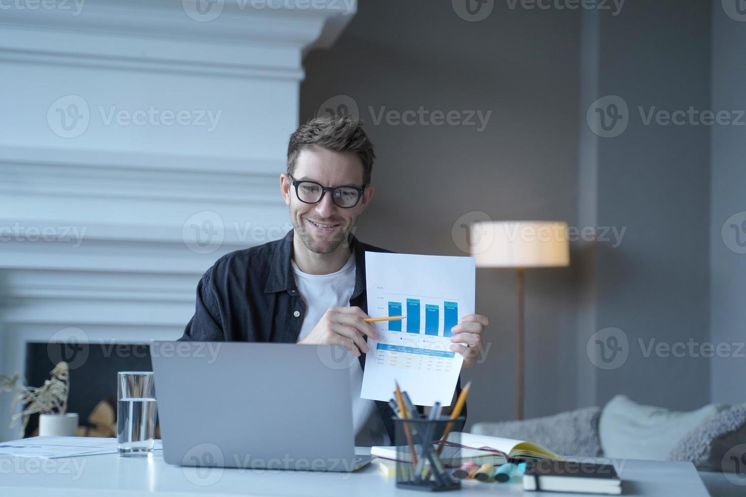 joven empresario alemán sonriente señalando un documento con gráficos durante una reunión en Internet foto
