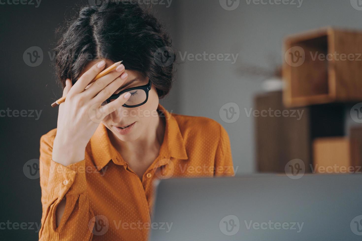 Frustrada y cansada joven española oficinista con gafas cubriendo la cara con la mano foto