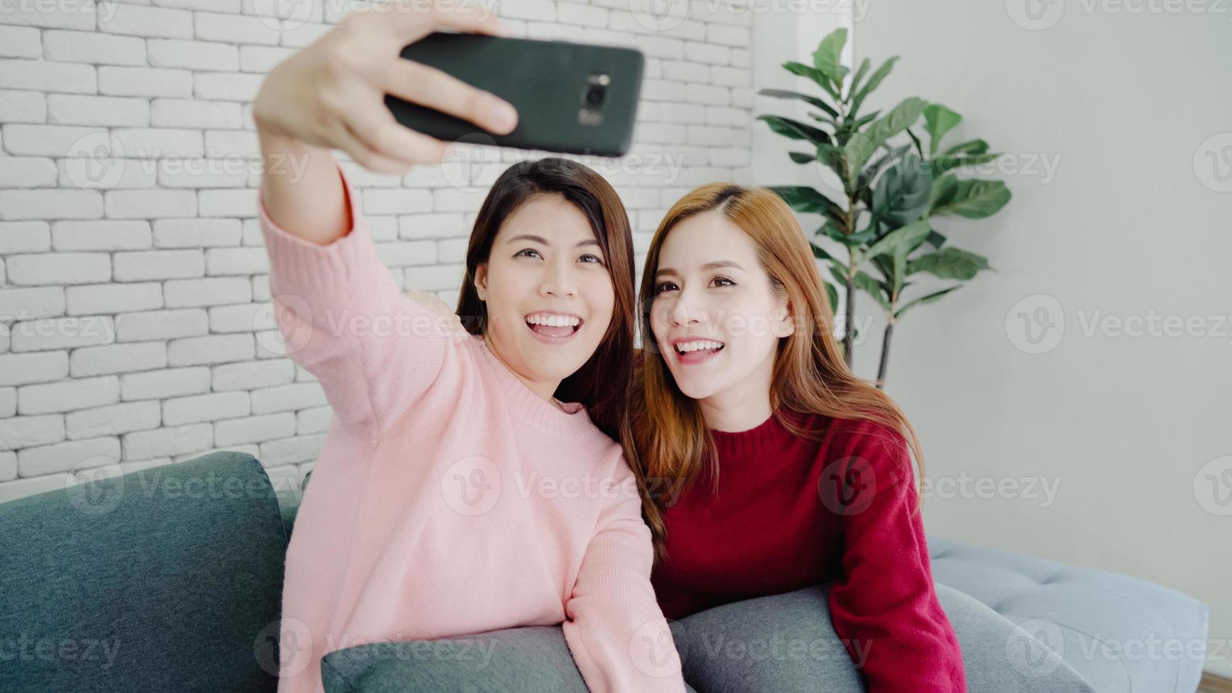 pareja lesbiana asiática usando selfie de smartphone en la sala de estar en casa, dulce pareja disfruta de un momento divertido mientras está acostado en el sofá cuando está relajado en casa. pareja de estilo de vida relajarse en el concepto de casa. foto