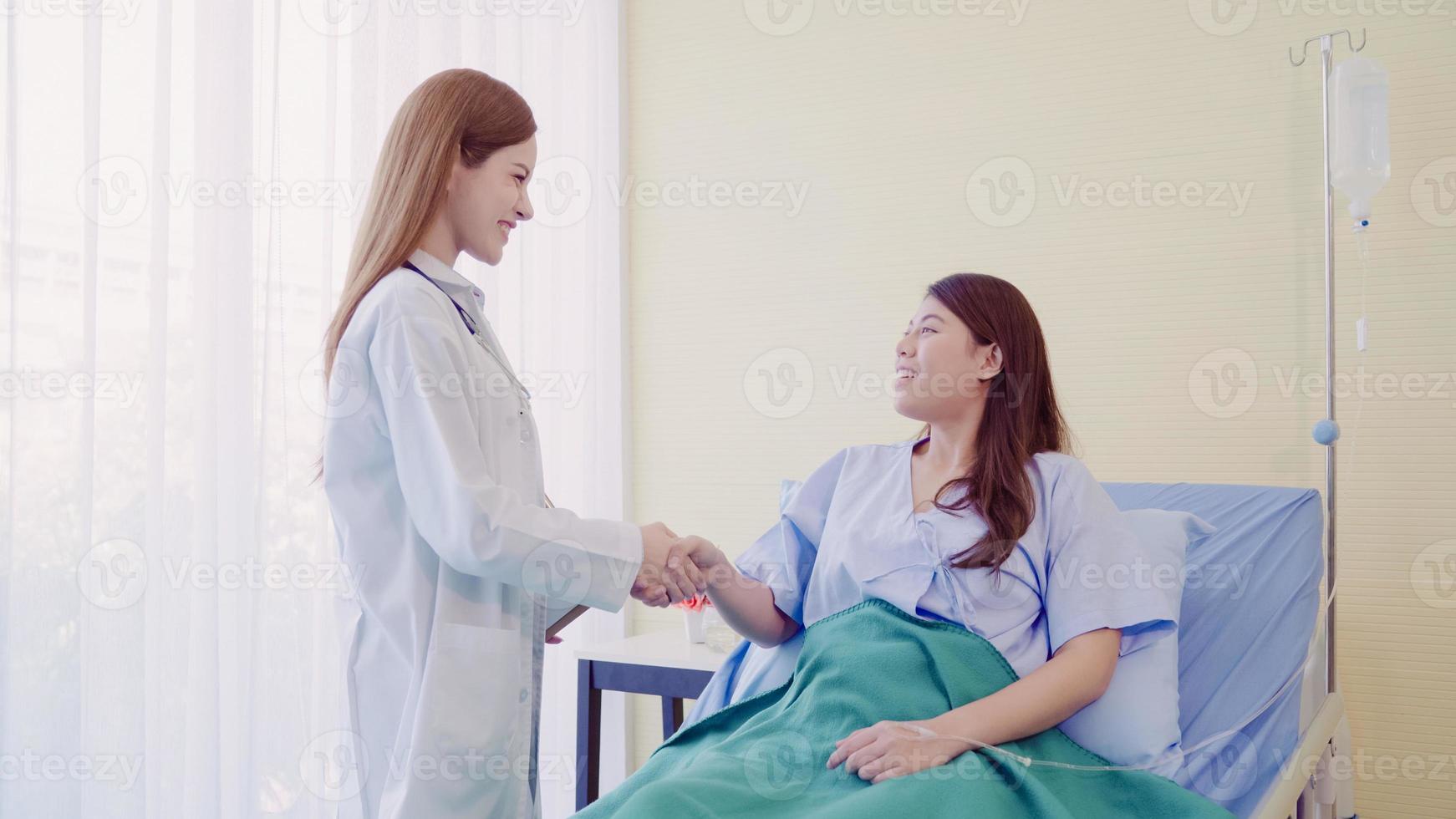 Young Asian doctor woman show information treatment on clipboard for women patient in sick bed. Medicine, age, healthcare and people concept. photo