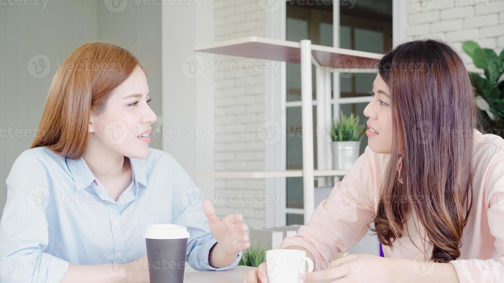 Asian business women enjoying drinking warm coffee, discuss about work and chit chat gossip while relax working in office. Smart business women social meeting concept. photo
