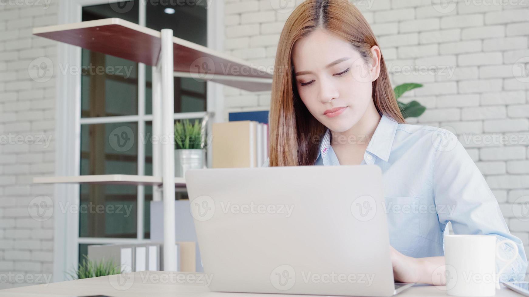 Beautiful young smiling asian woman working laptop on desk in living room at home. Asia business woman writing notebook document finance and calculator in home office. Enjoying time at home concept. photo