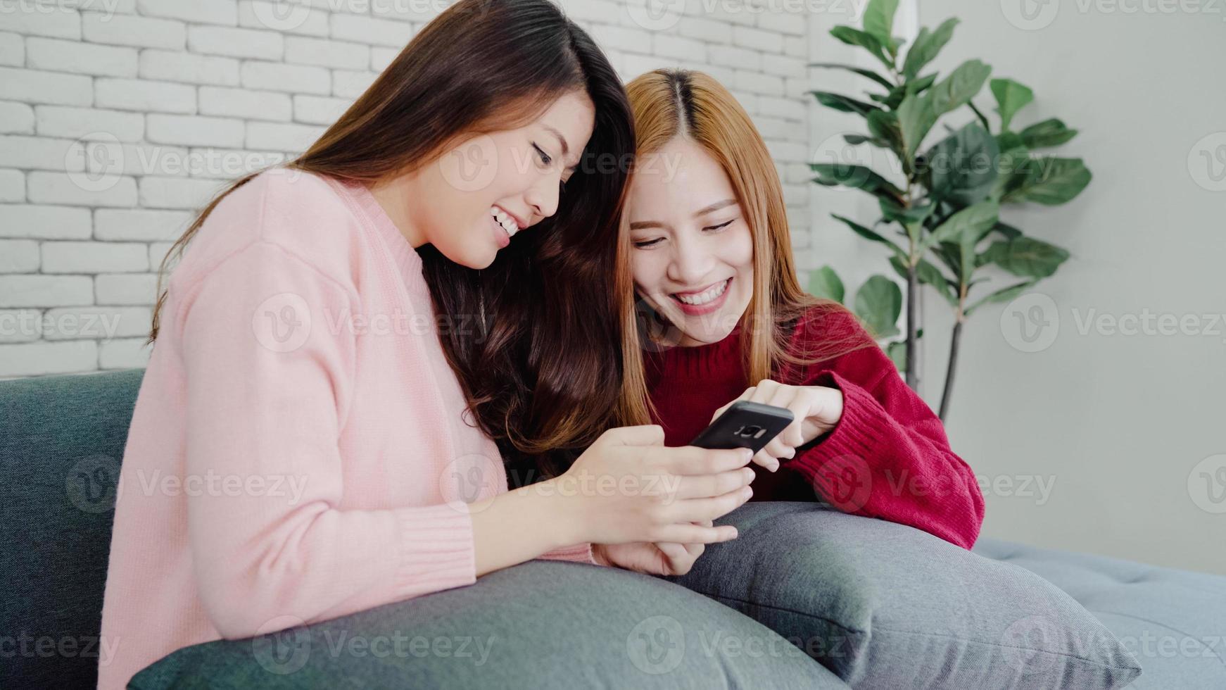 Asian women using smartphone checking social media in living room at home, group of roommate friend enjoy funny moment while lying on the sofa. Lifestyle women relax at home concept. photo