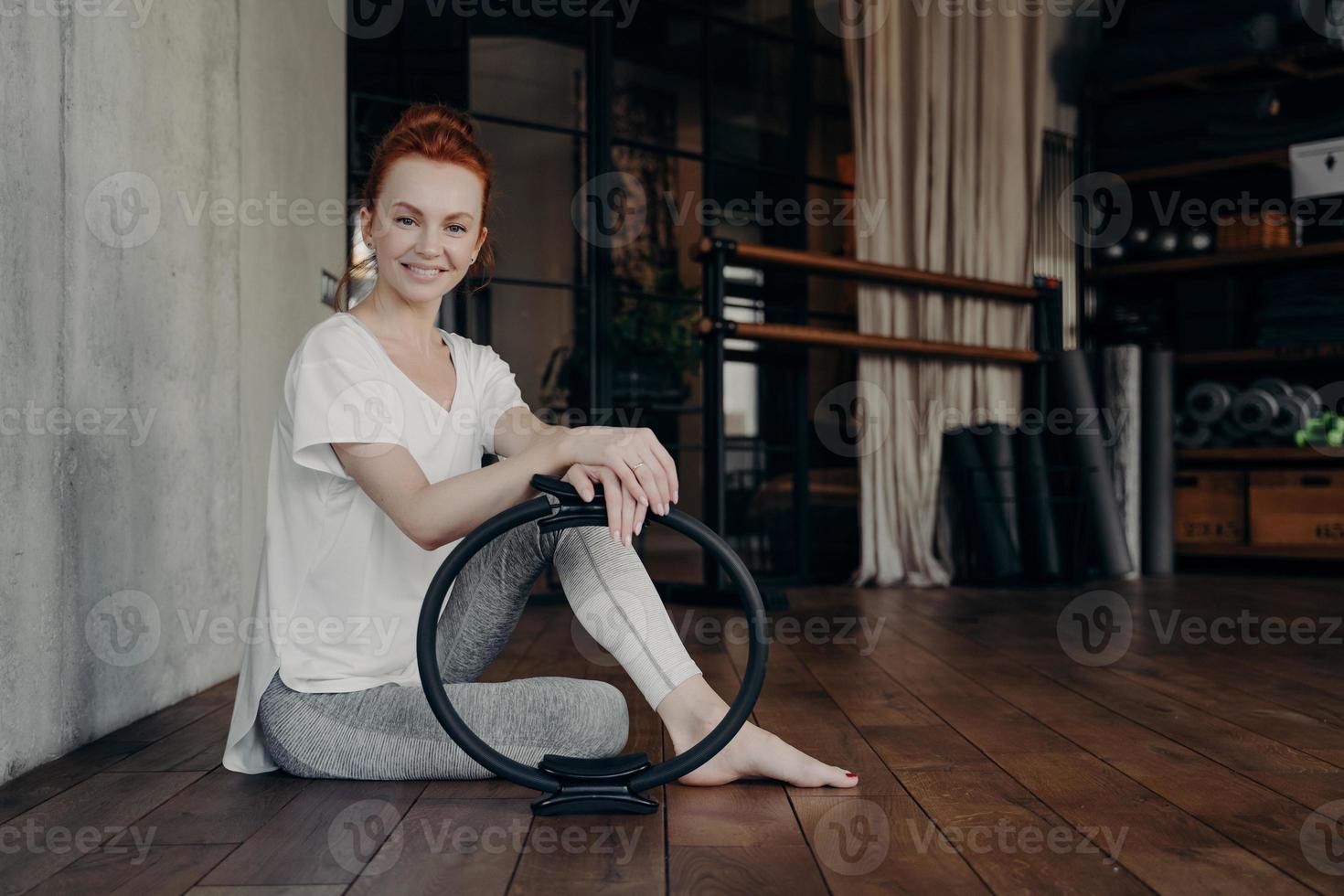 Smiling young sportive woman with pilates ring enjoying workout in fitness studio photo