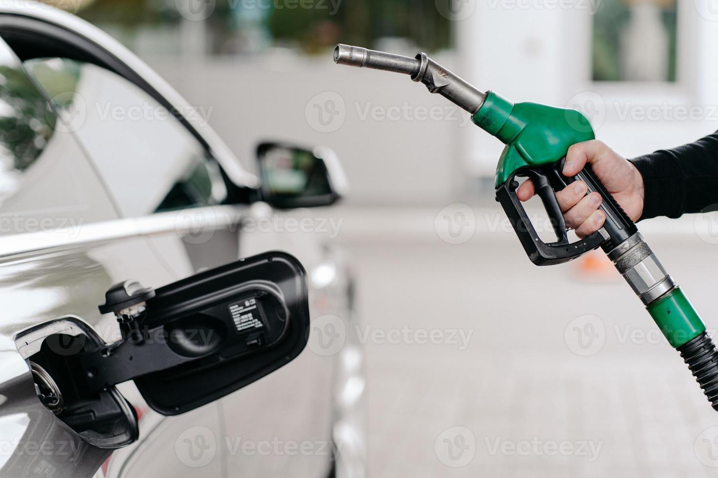 captura recortada de la mano del hombre bombeando combustible de gasolina en el coche en la gasolinera. auto siendo llenado con gasolina. el hombre irreconocible sostiene la boquilla de combustible. foto