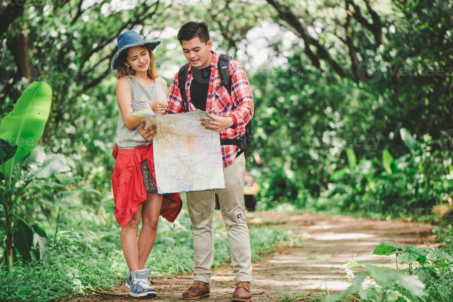Hiking - hikers looking at map. Couple or friends navigating together smiling happy during camping travel hike outdoors in forest. Young mixed race Asian woman and man. photo