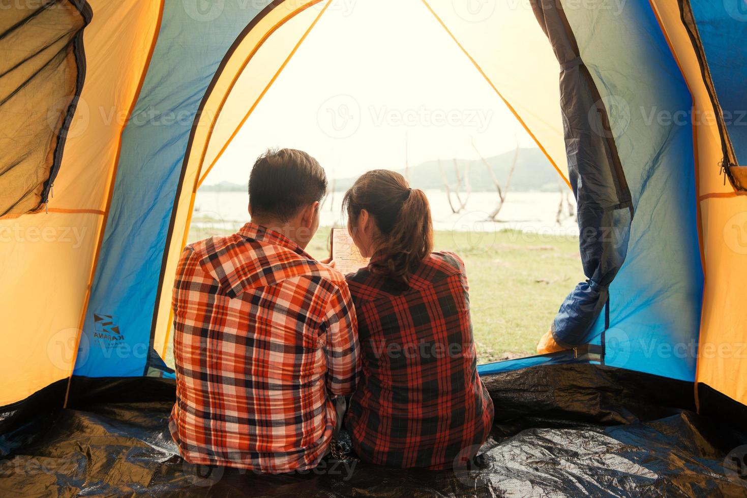 Tent carefree couple relaxing remote travel concept - Couple of young backpackers sitting in a tent looking at book and planning their next camping adventure photo