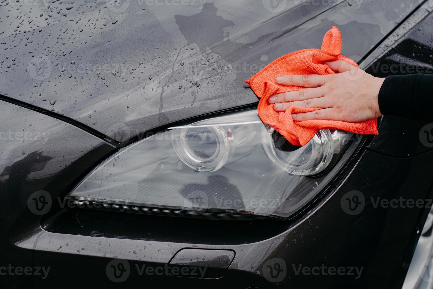 mans mano con trapo limpiando los faros de los coches. Limpie el automóvil negro húmedo en el lavado de autos. concepto de servicio y limpieza automática foto