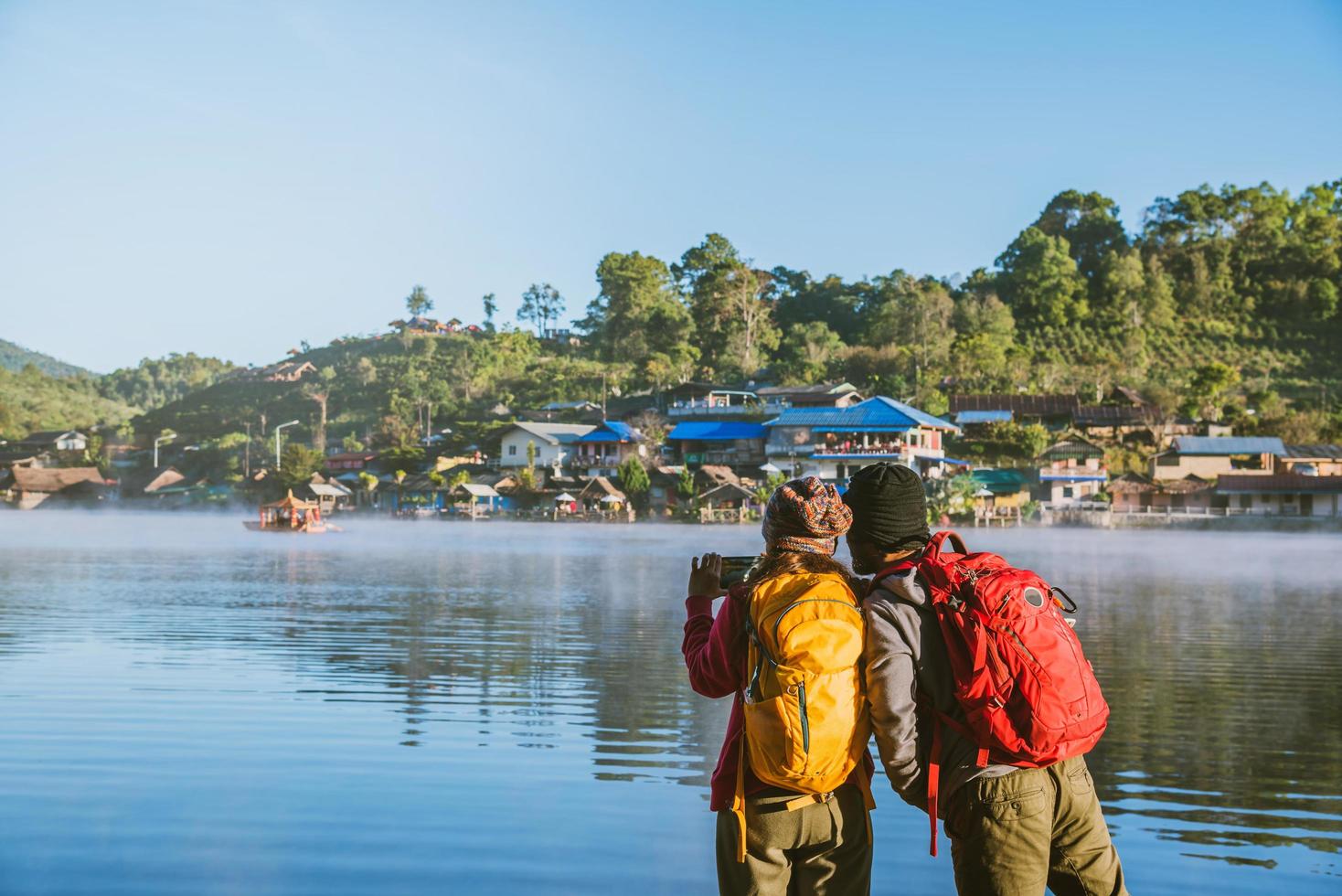 An Asian couple who is standing and watching the fog rising on the lake in the morning, Travel nature. Take a picture of the lake. photo