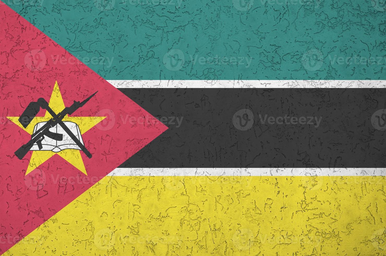 Mozambique flag depicted in bright paint colors on old relief plastering wall. Textured banner on rough background photo