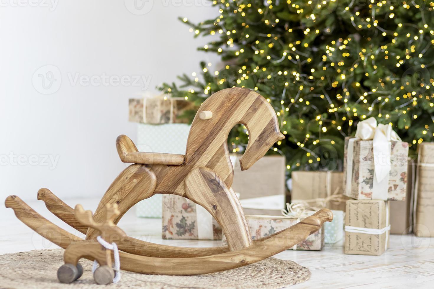 Cozy New Year's interior of the room, a children's horse and a Christmas tree are decorated with garlands, gifts, toys, candles, lanterns. Festive living room. New Year. photo