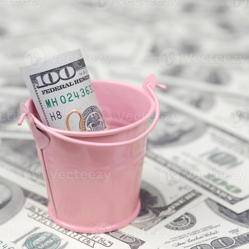 A bundle of US dollars in a metal pink bucket on a set of dollar bills photo