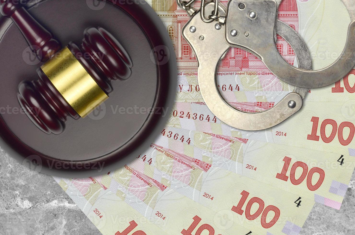 100 Ukrainian hryvnias bills and judge hammer with police handcuffs on court desk. Concept of judicial trial or bribery. Tax avoidance photo