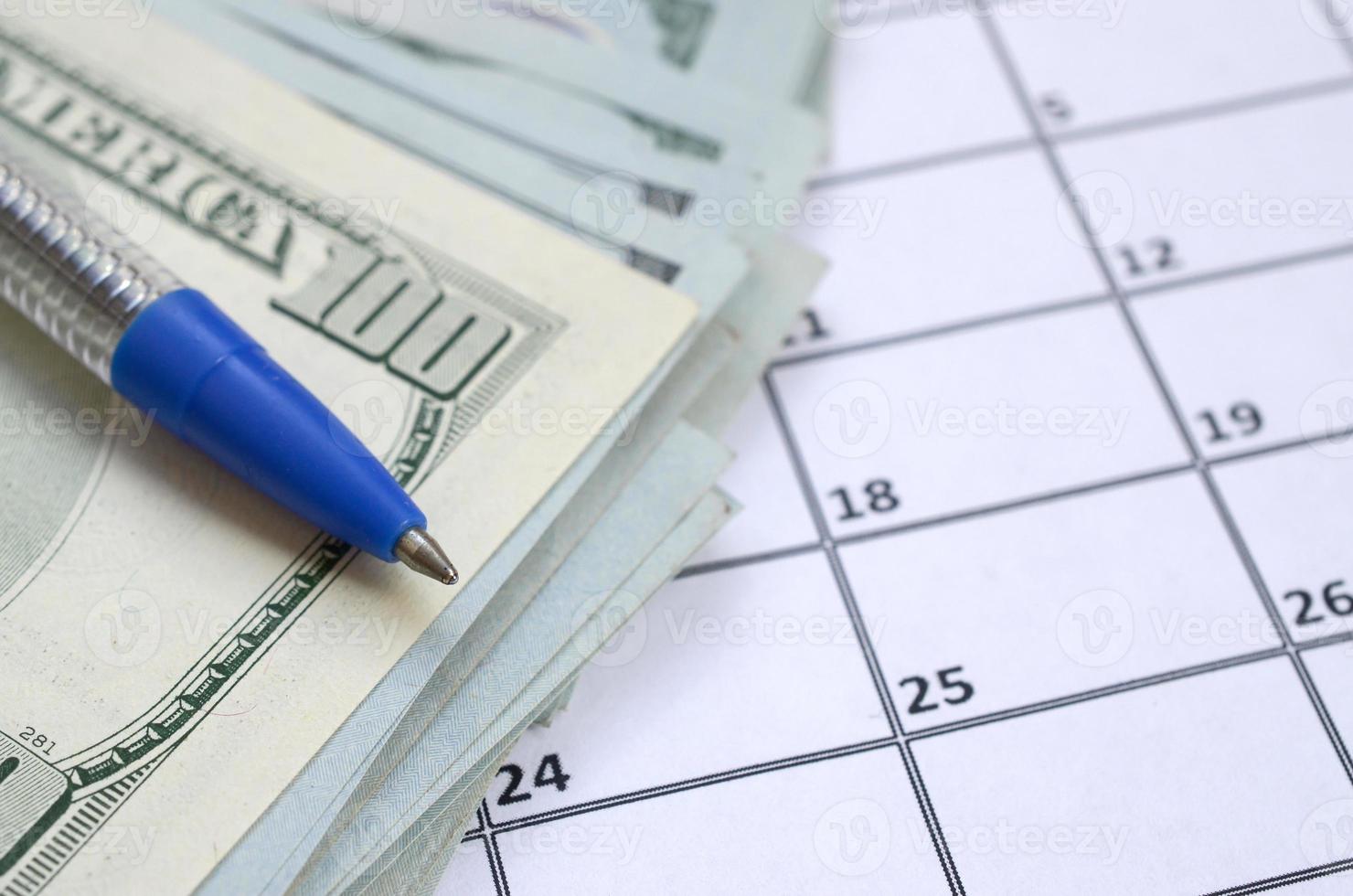 Pen and many hundred US dollar bills on calendar page close up photo