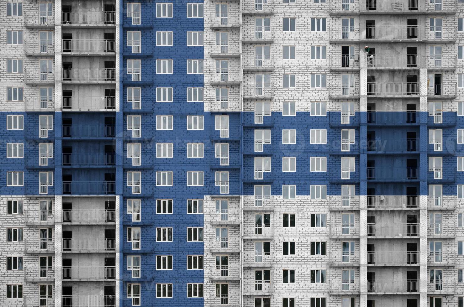 Finland flag depicted in paint colors on multi-storey residental building under construction. Textured banner on brick wall background photo