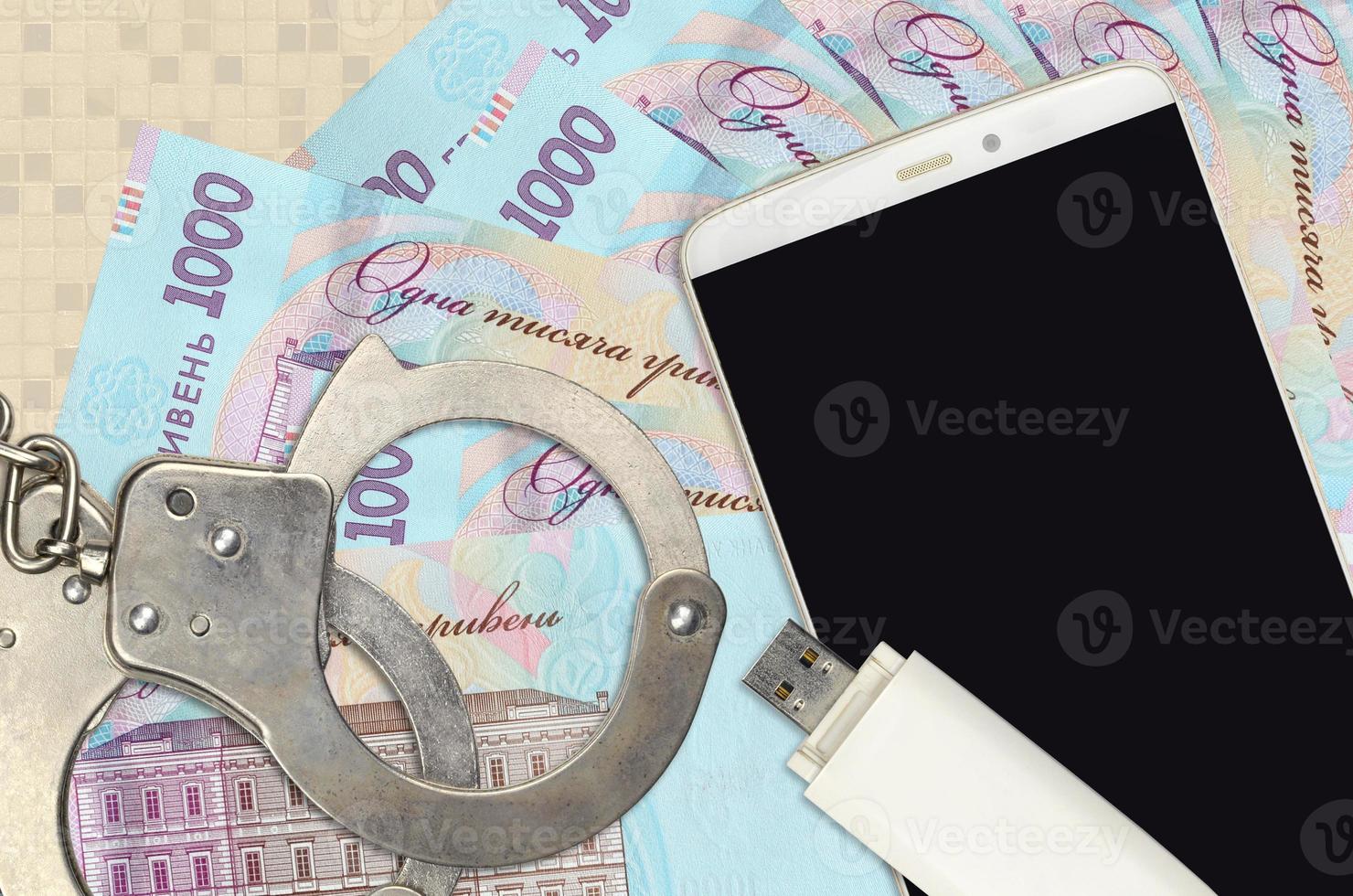 1000 Ukrainian hryvnias bills and smartphone with police handcuffs. Concept of hackers phishing attacks, illegal scam or malware soft distribution photo