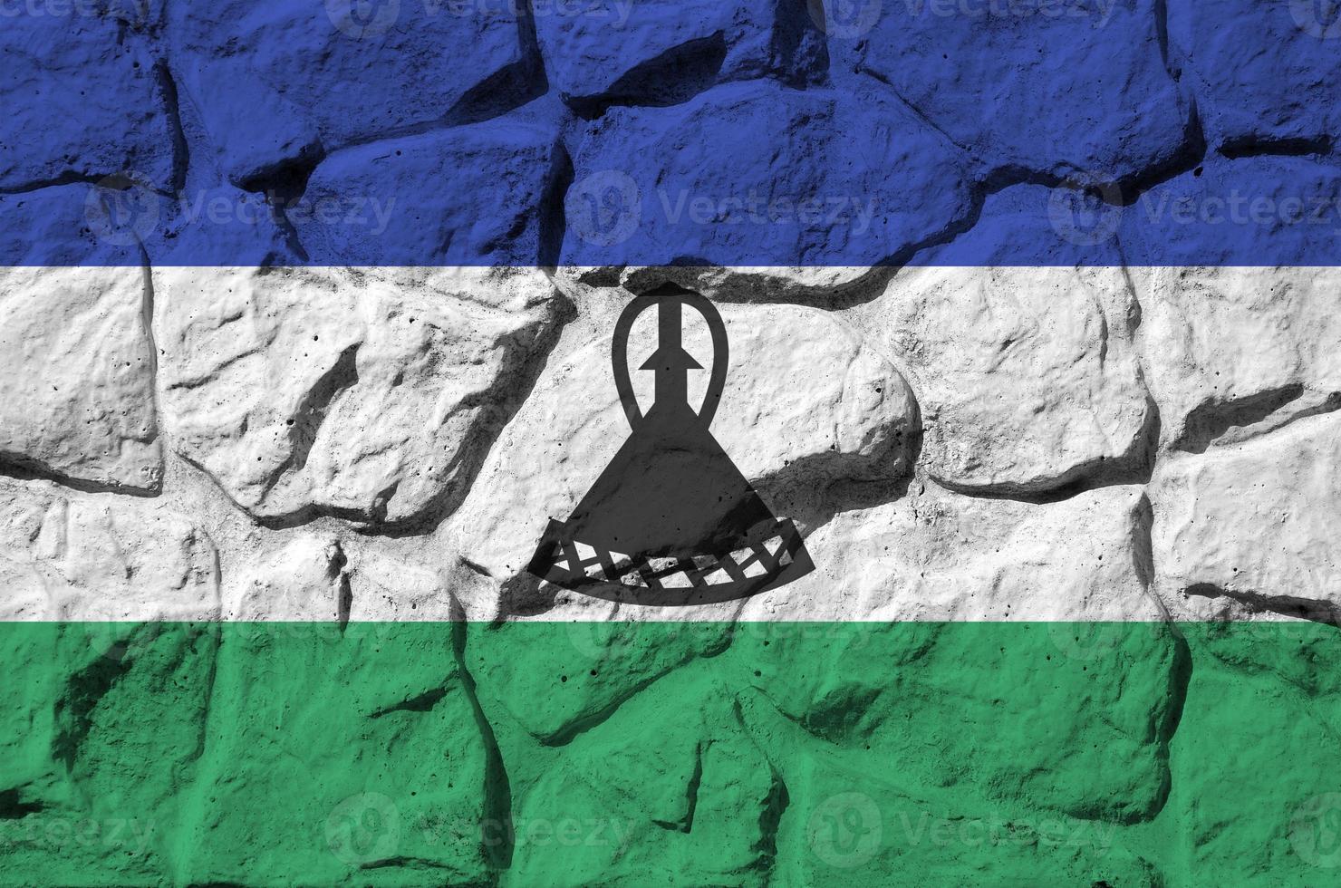 Lesotho flag depicted in paint colors on old stone wall closeup. Textured banner on rock wall background photo