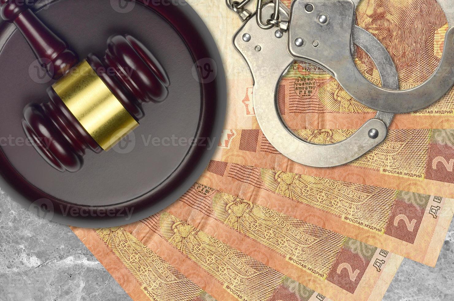 2 Ukrainian hryvnias bills and judge hammer with police handcuffs on court desk. Concept of judicial trial or bribery. Tax avoidance photo